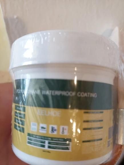 Small white container of waterproof glue for bathrooms with yellow and green label held in hand