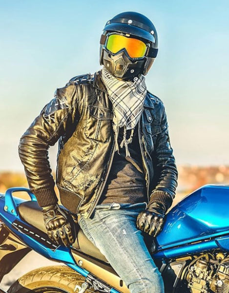 Stylish rider wearing motorcycle protective goggles and a leather jacket on a blue motorcycle