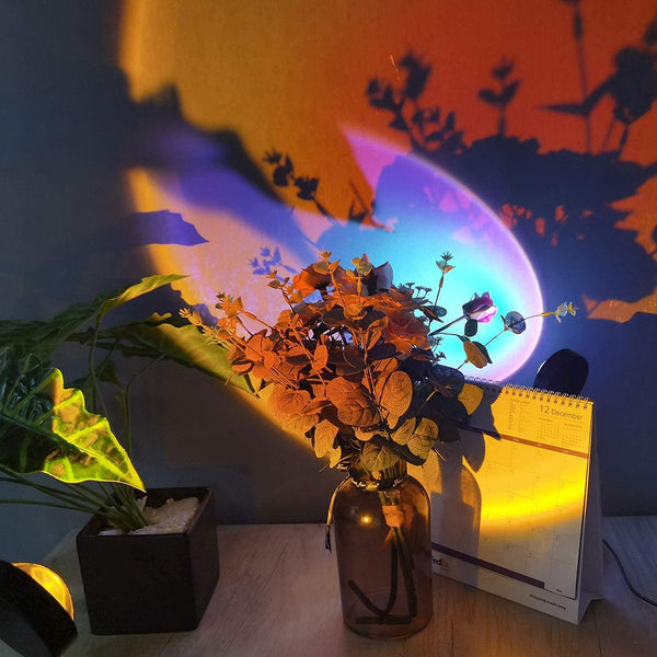 Sunset projection lamp 16 colors casting vibrant shadows on a vase with flowers and a calendar