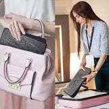 Woman placing EMS foot massager pad with geometric pattern into a pink handbag and holding it near a suitcase
